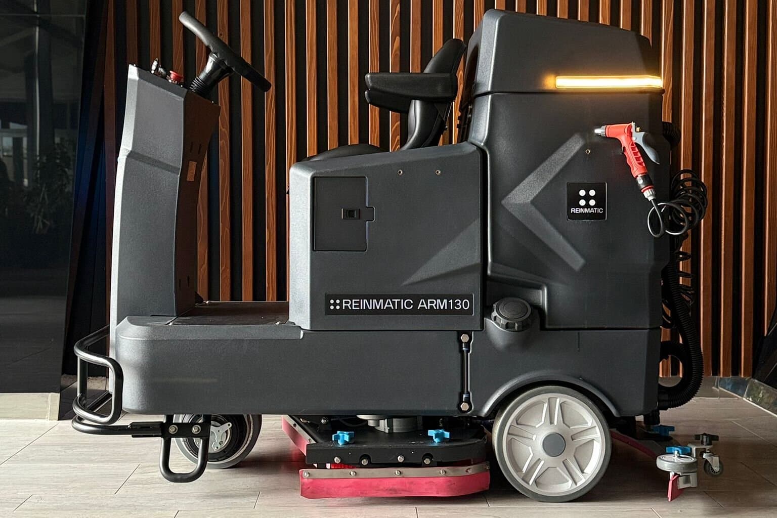 Full side profile of the ARM 130 with the REINMATIC ARM130 label — brush deck and squeegee visible beneath the chassis