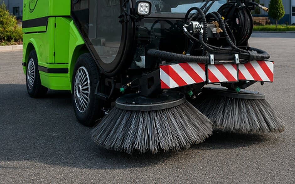 Twin front brushes of the REINMATIC SRM 1850 with red-and-white striped bumper plates on dry asphalt